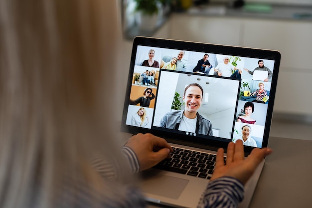 Vista posterior de la mujer de negocios hablando con sus colegas sobre el plan en la videoconferencia. Equipo de negocios multiétnico usando laptop para una reunión en línea en videollamada. Grupo de personas inteligentes que trabajan desde casa