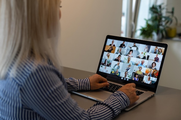 Vista posterior de la mujer de negocios hablando con sus colegas sobre el plan en la videoconferencia. Equipo de negocios multiétnico usando laptop para una reunión en línea en videollamada. Grupo de personas inteligentes que trabajan desde casa