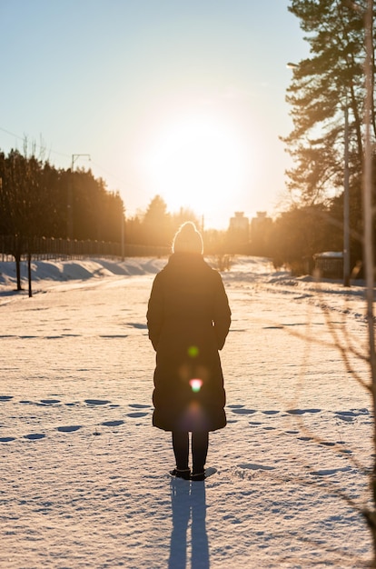 Vista posterior de la mujer de pie en la nieve y mirando la luz del sol Ambiente de invierno tranquilo Pasar tiempo a solas