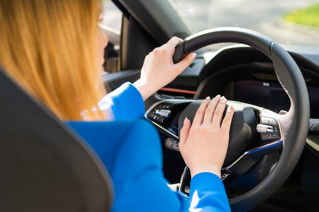 Vista posterior de la mujer que conduce un automóvil y presiona la bocina del vehículo con traje azul