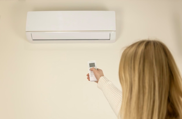 Vista posterior de una mujer que controla la temperatura del aire en la casa con un control remoto Concepto de aire acondicionado doméstico