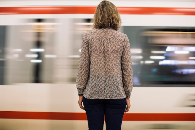 Vista posterior de una mujer rubia esperando en la plataforma del tren