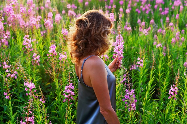 Vista posterior de la mujer rubia en la pradera fireweed