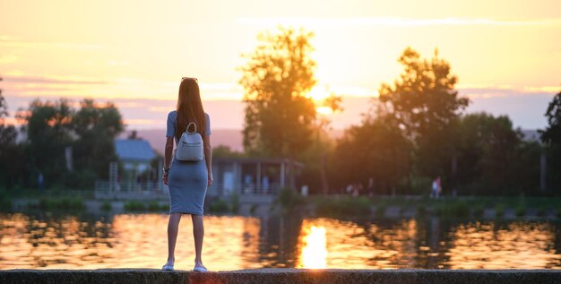 Vista posterior de la mujer solitaria de pie al lado del lago en una cálida noche. Concepto de soledad y relajación.