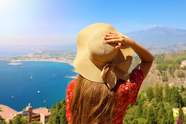 Vista posterior de la mujer turista con sombrero disfrutando de la vista del paisaje siciliano desde la ciudad de Taormina en Sicilia, Italia.