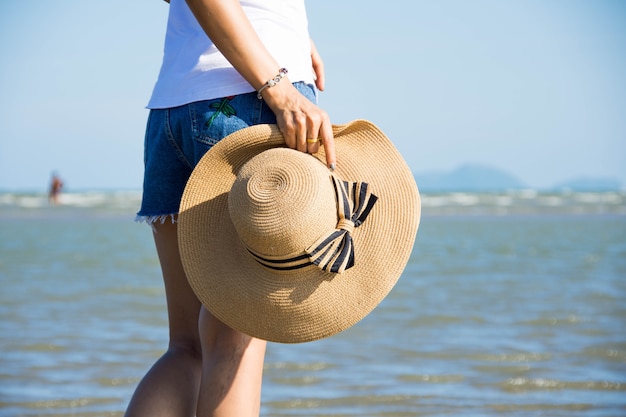 vista posterior de la mujer use sombrero soporte en la playa con cielo azul en un día soleado