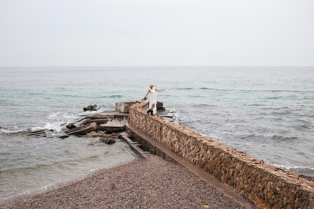 Vista posterior de la mujer con vestido blanco cerca del mar en otoño