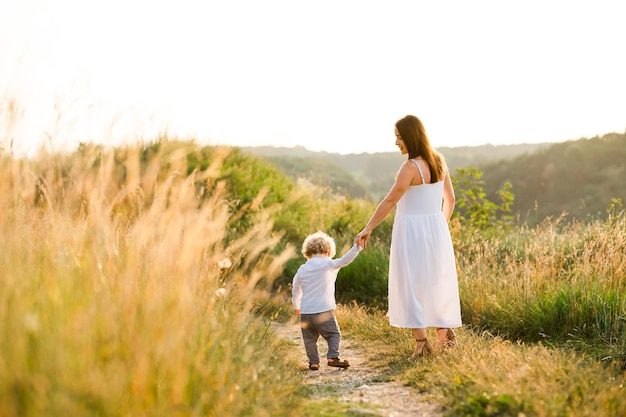 Vista posterior de la mujer en vestido ligero de verano camina con su hijo