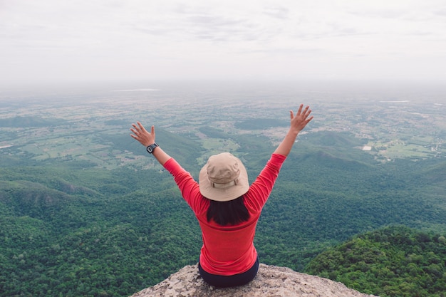 Vista posterior de las mujeres sentadas en el acantilado y empujar las manos contra la montaña y el árbol