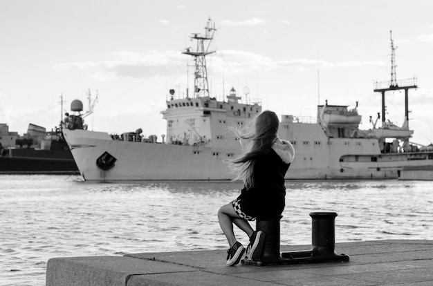 Vista posterior de la niña mirando los barcos. Mujer soñando con viajes por mar.