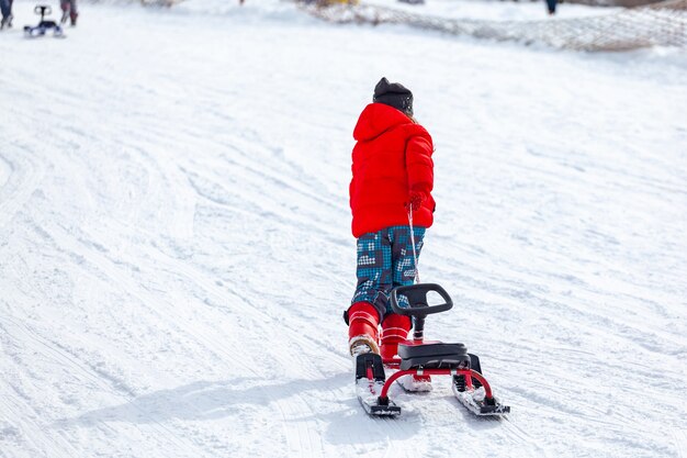 Vista posterior del niño tirando del trineo y corriendo cuesta arriba nevada mientras pasa tiempo en la estación de esquí