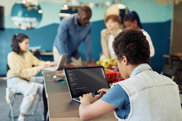 Foto vista posterior del niño usando una computadora portátil en clase de ingeniería y espacio de copia de robots de programación