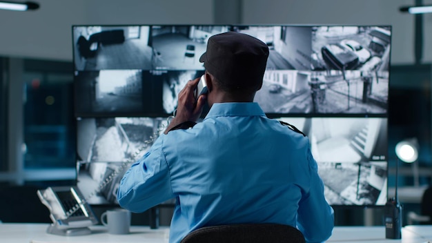 Vista posterior del oficial de seguridad afroamericano en la sala de control del sistema contesta la llamada telefónica