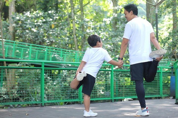 Vista posterior de padre e hijo se toman de la mano mientras estiran las piernas, hacen ejercicio y pasan tiempo juntos en