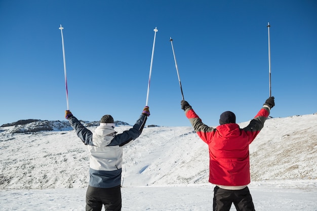 Vista posterior de una pareja levantando bastones de esquí en la nieve