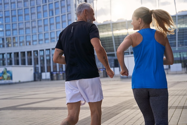 Vista posterior de la pareja de mediana edad en ropa deportiva llena de energía para correr juntos en el entorno urbano