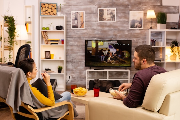 Vista posterior de la pareja en la sala de estar viendo una película en la televisión mientras come comida para llevar