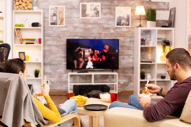 Vista posterior de la pareja en la sala de estar viendo una película en la televisión mientras come comida para llevar