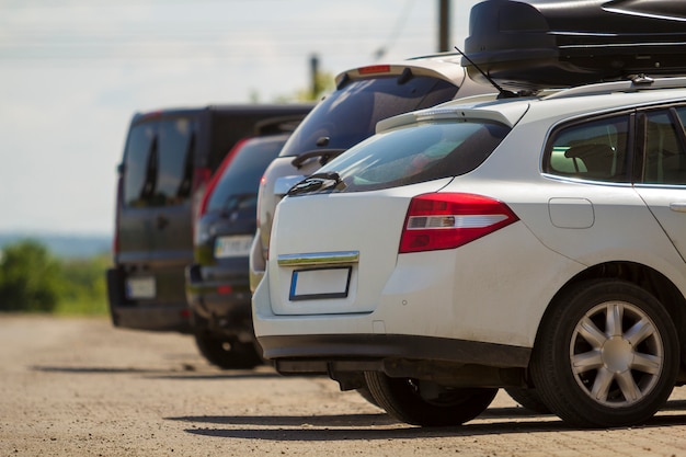 Foto vista posterior de primer plano del caro coche moderno blanco con baúl negro en el techo en la fila de automóviles y furgonetas estacionadas sobre asfalto en un día soleado. concepto de transporte y estacionamiento.