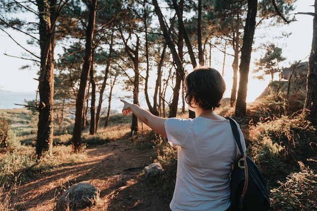 Vista posterior puesta de sol joven camina por el camino de las rocas en la orilla y mira el mar de la noche.Hombre joven inconformista haciendo algunas caminatas en la orilla, viajes y conceptos de viaje de bajo presupuesto, espacio de copia