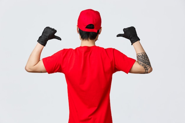 Vista posterior del repartidor con gorra roja y camiseta, con guantes protectores durante la pandemia covid-19.