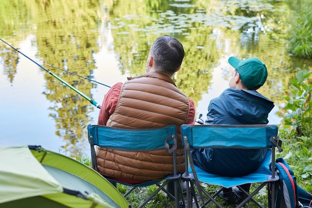 Vista posterior retrato de amoroso padre e hijo pescando juntos durante el viaje de campamento por el lago, espacio de copia