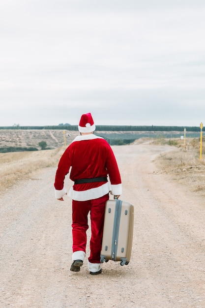 Vista posterior de Santa Claus con una maleta de viaje en un paisaje rural. Viajar en concepto de Navidad