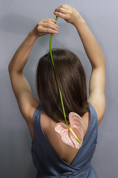 Vista posterior sensual retrato de niña morena de pelo largo con flor rosa Anthurium sobre fondo gris