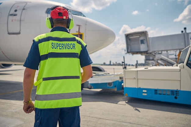 Vista posterior de un supervisor con un chaleco reflectante parado frente al vehículo aéreo