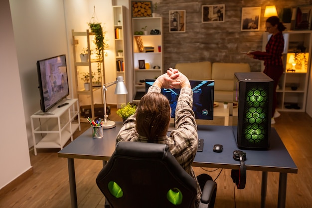 Foto vista posterior del videojugador profesional que juega en una potente pc a altas horas de la noche en la sala de estar.