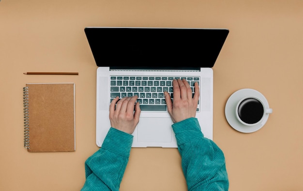 Vista de POV en las manos femeninas sobre la computadora portátil junto a la taza de café y el cuaderno sobre fondo marrón