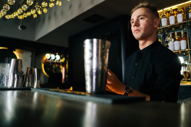 Vista de primer plano de un barman confiado que hace un refrescante cóctel alcohólico de pie detrás del mostrador del bar en un moderno club nocturno oscuro