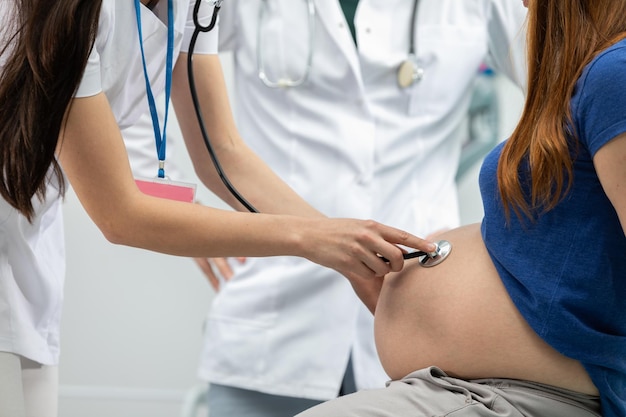 Vista en primer plano de una doctora auscultando el abdomen de una mujer embarazada con un estetoscopio Oficina de médicos profesionales
