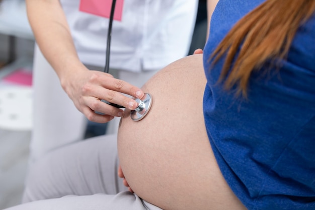 Vista en primer plano de una doctora auscultando el abdomen de una mujer embarazada con un estetoscopio