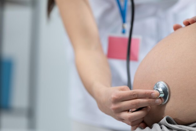 Foto vista en primer plano de una doctora auscultando el abdomen de una mujer embarazada con un estetoscopio