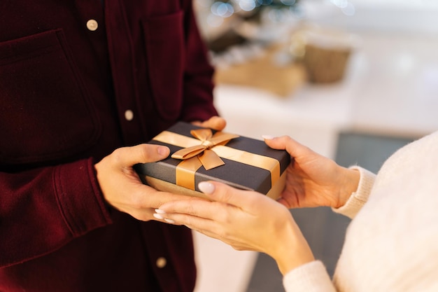 Vista de primer plano de un joven amoroso irreconocible que presenta una caja de regalo a una mujer feliz en el salón del centro comercial Celebra