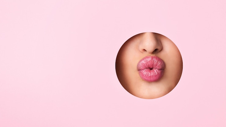 Foto una vista en primer plano de los labios de una mujer que sobresalen de un agujero contra un fondo rosado vibrante