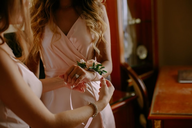 La vista de primer plano de las manos de las novias atando la pulsera de la boda en la mano de la dama de honor.