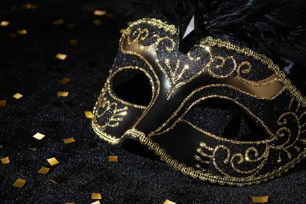 Foto vista en primer plano de la máscara de oro de masquerade con plumas y confeti sobre fondo negro