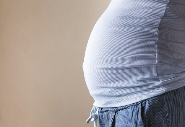 Una vista de primer plano del vientre de una mujer embarazada en una camiseta blanca.