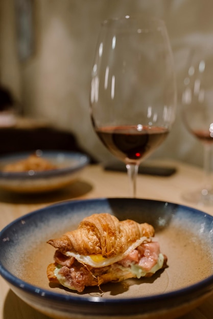 Vista próxima de um croissant de atum vermelho com ovo e um copo de vinho