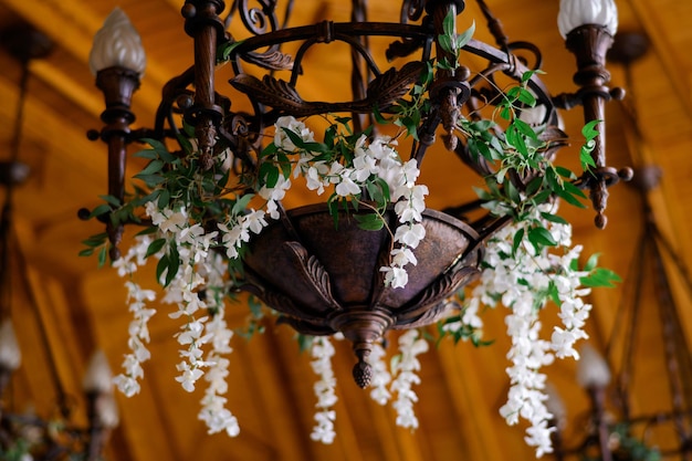 Vista próxima do candelabro antigo e forjado com castiçal decorado por flores brancas artificiais penduradas no teto de madeira no grande salão