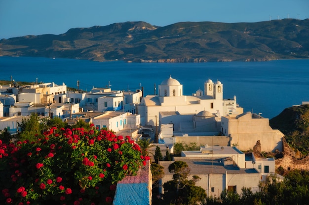 Vista del pueblo de plaka en la isla de milos sobre flores de geranio rojo al atardecer en grecia