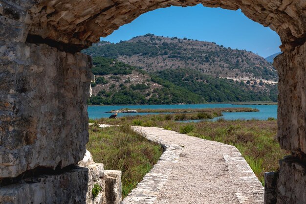 Foto vista desde la puerta del arco del castillo de ali pasha junto al lago butrint con montañas verdes en ksamil albania