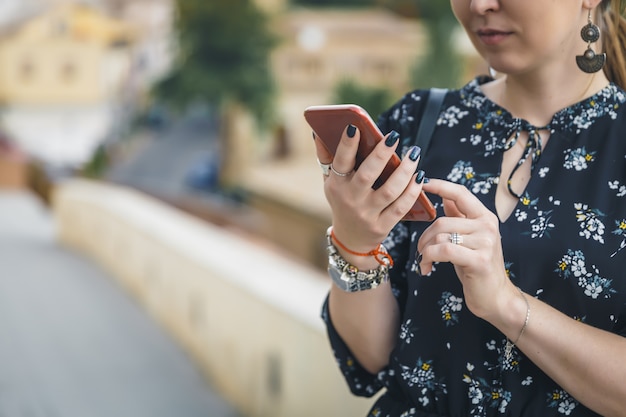 Vista recortada de bastante joven en un vestido negro con smartphone en la calle de la ciudad vieja.