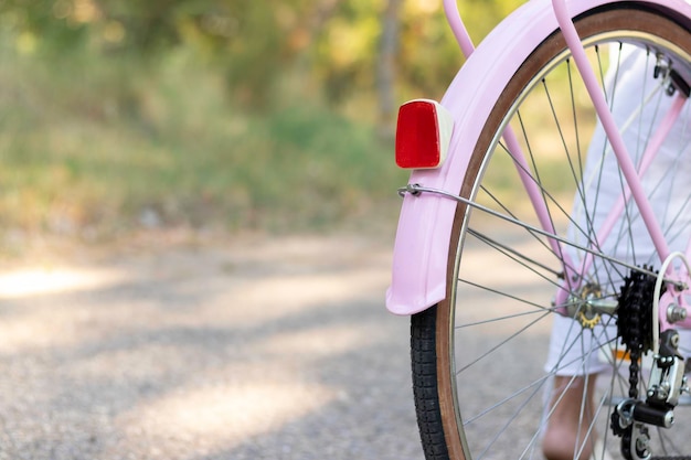 Vista recortada de una bicicleta rosa desde atrás con una mujer montándola en la carretera con la naturaleza