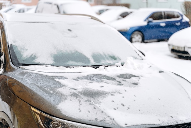 Vista recortada del capó del coche bajo la nieve después de una nevada. Autos en el estacionamiento cubierto de nieve. Invierno nevado y mucha nieve concepto