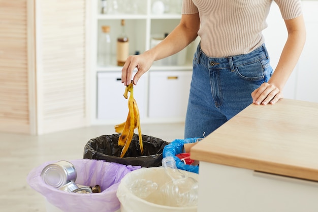 Vista recortada de mulher colocando casca de banana na lata de lixo. lixeiras diferentes para separar o lixo na cozinha