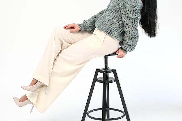 Vista recortada de uma mulher estilosa em calças brancas sentada em uma cadeira preta de madeira sobre fundo branco