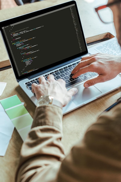 Vista recortada del desarrollador que trabaja con una computadora portátil en la mesa en el espacio de coworking